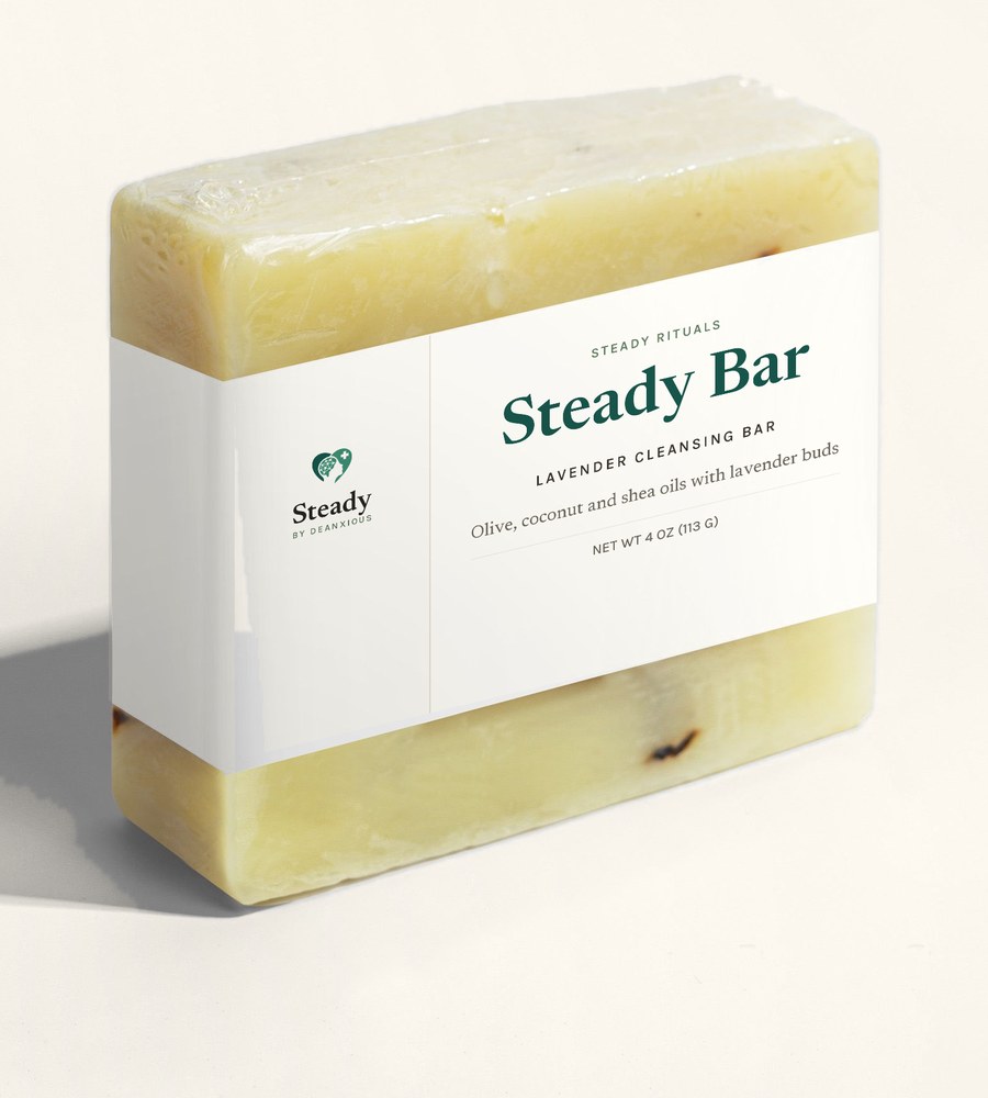 Steady Bar: a pale wrapped cleansing bar flecked with lavender buds, banded with a cream Steady label, on a warm cream ground.